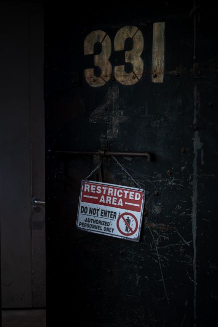 A dark, industrial-style door with large white numbering '331' at the top. A red and white 'Restricted Area' sign hangs from a metal bar attached to the door, indicating 'DO NOT ENTER' and 'AUTHORIZED PERSONNEL ONLY,' with a crossed-out person symbol. The door surface shows scratches and wear, suggesting a secure or restricted section of a building. The surrounding environment appears to be part of a warehouse or storage facility, relevant to home relocation or removals service contexts where secure access is necessary during the logistics of furniture transport and moving processes. The image emphasizes secure areas involved in property transfers or storage handling, aligning with professional removals activities.